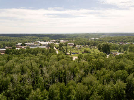 Forest in the Novosibirsk city,Siberia with diffrent trees and plants with some buildings in it and blue sky and clouds. Aerial view form a drone.の写真素材
