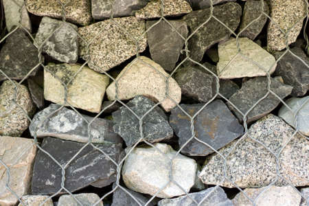 Gray stones stacked in the form of a wall and reinforced with iron grating. Light background of gravelの写真素材