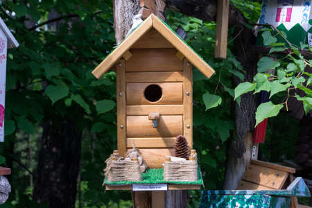 A wooden birdhouse made by children  for the exhibition in which the birds live, with green roof  and cone against the background of green leavesの写真素材