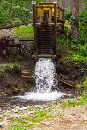 Vertical view on an old water mill in the mountains of the Altai producing electricity, through which water flows forming a waterfall spraying dropsの写真素材
