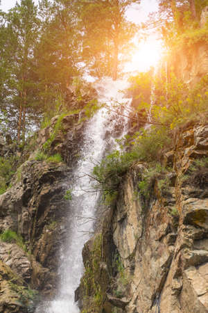 Vertical view to a high waterfall in the mountains of the Altai with sprinkled drops of water...