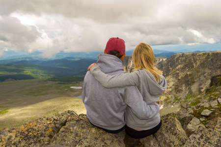 A loving couple sitting on the edge of a rock embraces in front of them a picturesque view