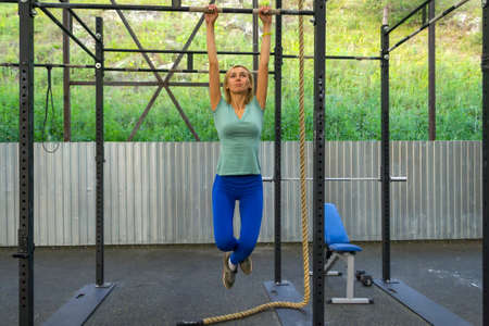 Blonde girl in blue leggings and a T-shirt keeps his arms outstretched for the horizontal bar...