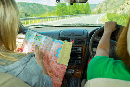 Two young woman travelling by car one in the passenger seat looks at the paper map looking for the...