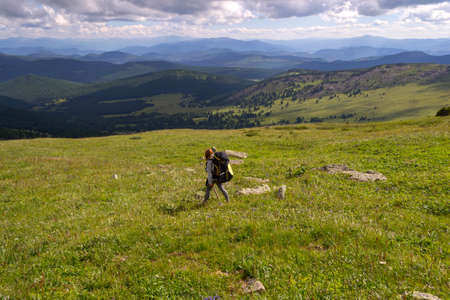 A girl tourist in a hood,with a large backpack and a wooden stick in her hands descends from the...