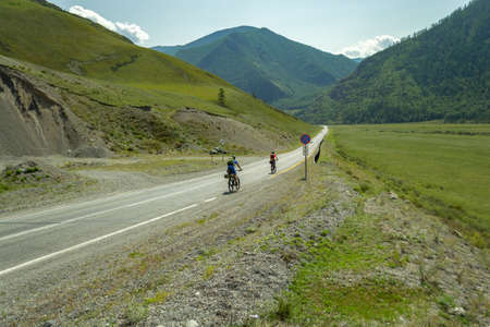A couple of man and woman in helmets ride on sports bicycles on a road in the mountains of the Altai climbing upの写真素材
