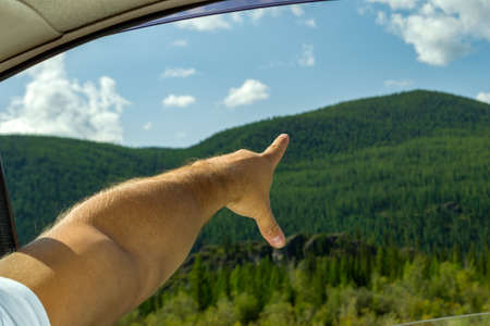 The man's arm, covered with hair, is open, showing by the finger to the peak of the mountain on the...