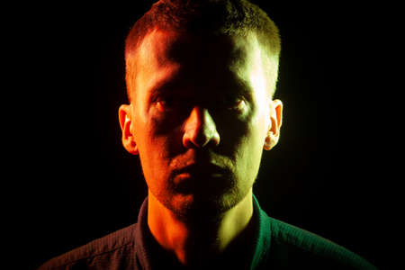 Close-up of the face of an unshaven face of a man with stubble, dressed in a shirt in the dark,...
