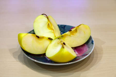 A green apple cut into four pieces on a colored plate after harvest in the fall. Fresh fruits for...