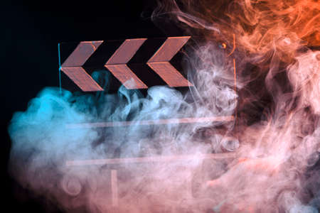 Black and white clapperboard for cinema close up among multicolored red and green smoke in a...