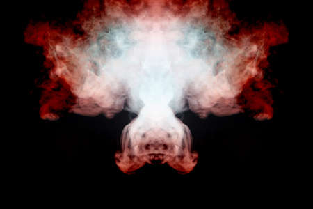 A mystical pattern of colored smoke of red and white in the shape of a ghost's face with fangs creating a feeling of fear on a black isolated background from a horror movie.の写真素材