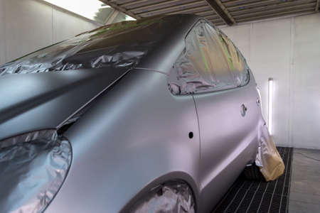 Full painting of the car in the back of a silver hatchback window and the wheels of which are covered with paper from hitting the paint in a special camera for body repair of vehicles in the workshopの写真素材