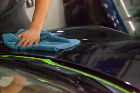 The mechanic in the service station polishes the car body, wiping with a napkin a glossy, shiny,...