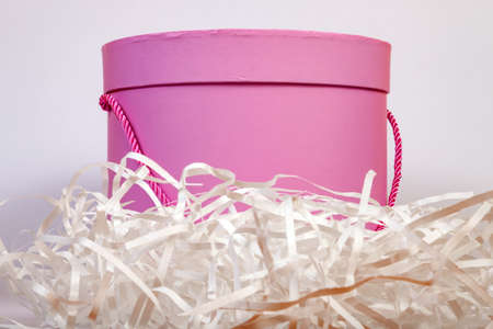 A pink round cardboard gift box is lined with paper shavings outside for packing buy on a white...