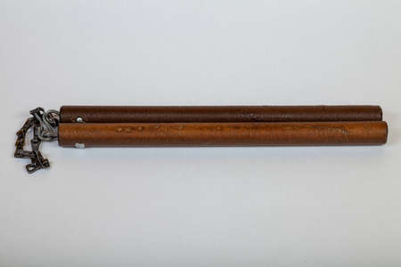 Close-up on vintage brown wooden nunchak connected by an iron chain, which lie horizontally on a...