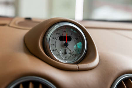 The watch on the dashboard of an expensive car is close-up, covered with natural beige leather, with...