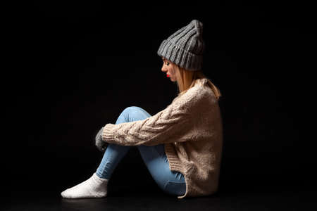 The girl is sitting alone on the floor on a black background of emptiness, hugging her legs with her hands and looking down, crying in a corner in a depressed state.の写真素材