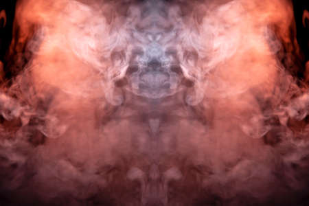 A mystical pattern of colored smoke of red and white in the shape of a ghost's face with fangs creating a feeling of fear on a black isolated background from a horror movie.の写真素材