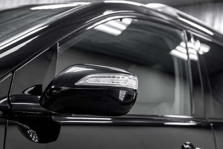 Close-up of the mirror of the car body  black sedan on the street parking in the snow.
