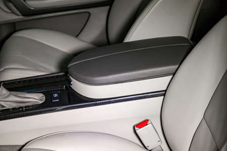 Close-up on the car front armrest with gray leather trim, buttons and seat belt in the interior...