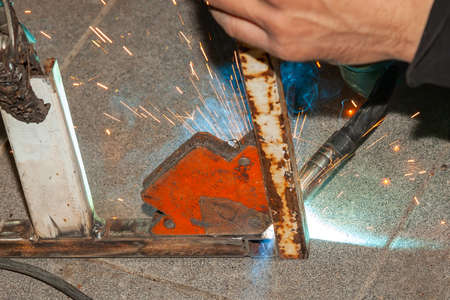 An experienced person performs work with a welding machine, fixing metal parts, removing blue smoke...