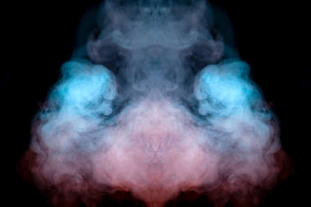 Mystical pattern of green, blue and pink colored smoke in the shape of a ghost's face with big eyes...