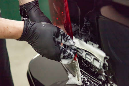 Thorough and painstaking washing of car parts in the form of emblems in a black glove with a sponge...