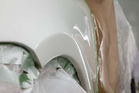 Painting the car body parts of the driver's white fender in the spray booth in the body repair shop,...