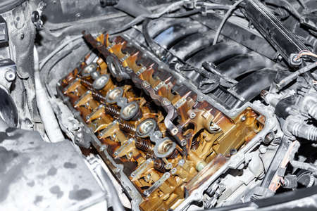 A six-cylinder in-line engine under the hood of the car with the valve cover removed with traces of...