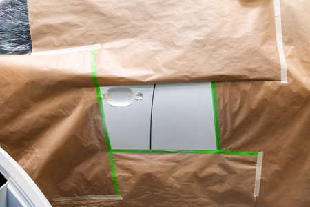 Parts of the car bumper and door after the accident in the camera for car body repair is partially covered with paper and pasted over with green masking tape for painting with white colorの写真素材