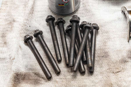 A handful of long bolts with a hat on a dirty white cloth in a repair shop. Industrial tool.