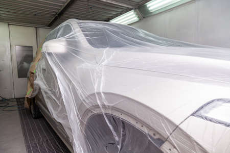 The car is a beige color covered with a transparent film to protect against the ingress of dirt and splashes from paint during body repair in the workshop for painting vehiclesの写真素材