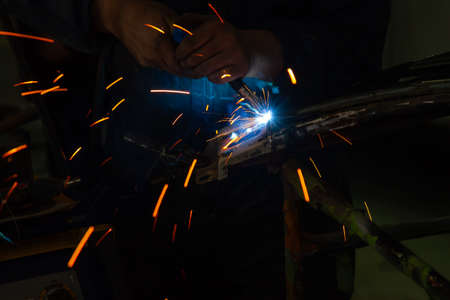 Close-up view strong man is a welder in blue working overalls without gloves on arms, a metal...