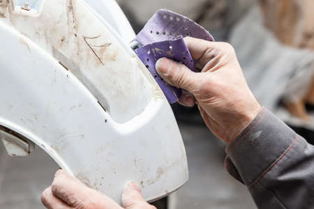 A man prepares a car body element for painting after an accident with the help of abrasive paper in...