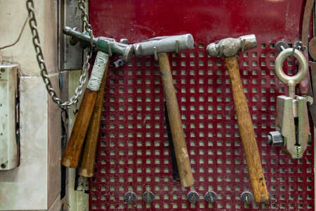 Four old hammers with a brown wooden handle and a clamp hang on the wall in the workshop for...