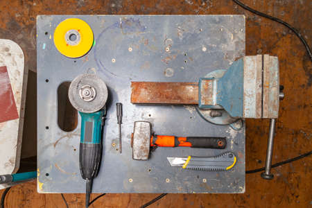 Flat lay view of a workbench with a set of tools consisting of a large heavy vise, angle grinder,...