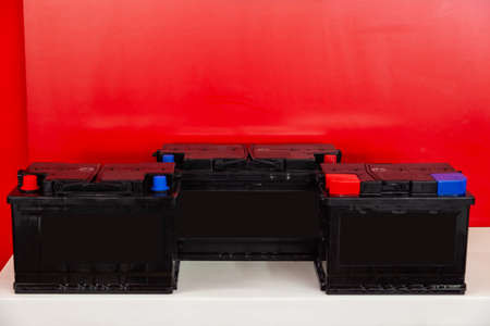 Three new black rechargeable batteries for car and vehicle stand  on a red background with white inscriptions. Auto service industry.の写真素材