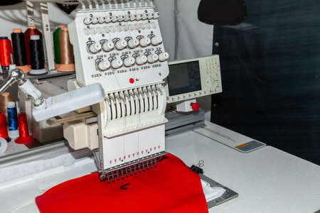Industrial white sewing machine for embroidery makes black logo with letter S  with black thread on...