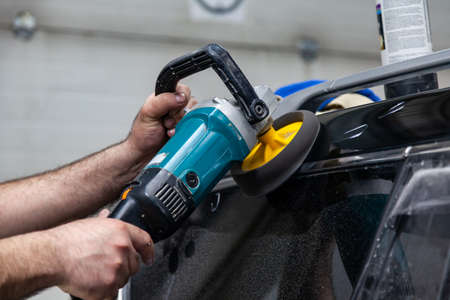Close-up view on the hands of a man worker who holds a tool polisher for polishing the roof of a car...