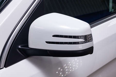 Close-up of the side left mirror with turn signal repeater and window of the car body white SUV on...