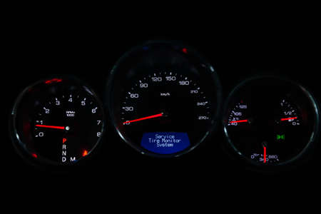 The dashboard of the car is glowing blue with red arrows at night with a speedometer, tachometer and...