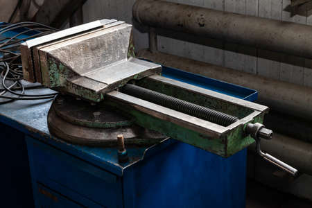Large and powerful green vise with overwhelmed paint on a blue workbench for metal and wood work in the workshop. Repair and carpentry in the industrial and manufacturing.の写真素材