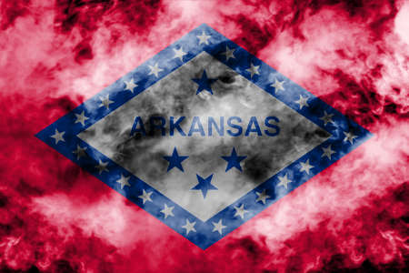 The national flag of the US state Arkansas in against a gray smoke on the day of independence in different colors of blue red and yellow. Political and religious disputes, customs and delivery.の写真素材