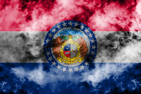 The national flag of the US state Missouri in against a gray smoke on the day of independence in different colors of blue red and yellow. Political and religious disputes, customs and delivery.の写真素材