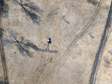 Aerial of Red tractor with a trailed plow for mowing and weeding fields for the agro-industry of...