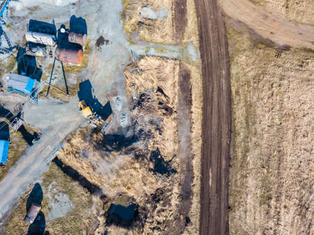 Aerial view of an excavator and yellow tractor transporting crushed stone, cement and sand during the extraction of minerals from the earth for the construction of roads and buildings on a sunny day.の写真素材