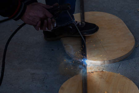 Close-up view strong man is a welder in blue working overalls without gloves on arms, a metal...