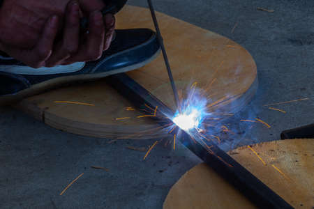 Close-up view strong man is a welder in blue working overalls without gloves on arms, a metal...