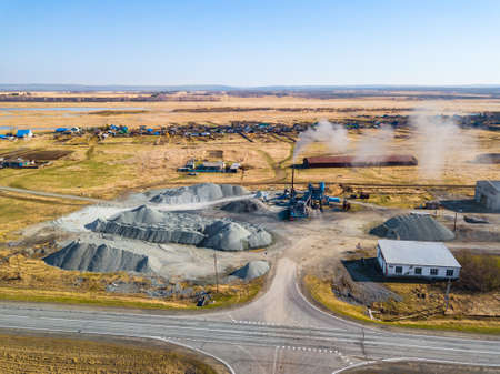 Aerial view of a small plant for the production and cleaning rubble and cement near the heaps of building materials from the pipe of which gray smoke goes, the tractor transports the finished product.の写真素材