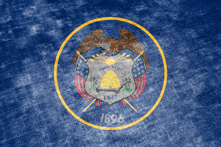 The national flag of the US state Utah in against a gray textile rag on the day of independence in different colors of blue red and yellow. Political and religious disputes, customs and delivery.の写真素材